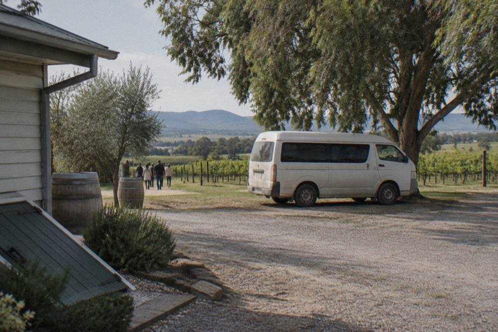 A small tour van parked beside a gravel driveway in front of a Hunter Valley cellar door